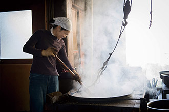 煉瓦のガス釜に三尺の平鍋を載せ、麦を手炒りする昔ながらの作業をする設楽徳子さん